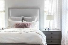 a glam bedroom with a light grey bed and neutral bedding, grey nightstands, a pink faux fur bench and a crystal chandelier