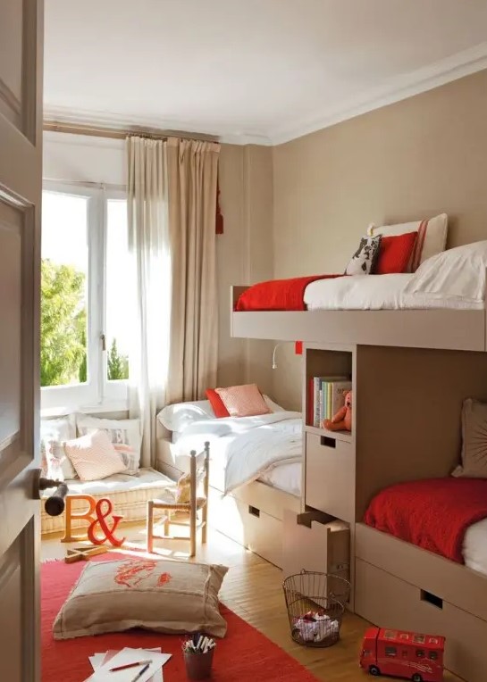 a greige kids' room with four bunk beds, a cushion with pillows on the floor and some bright red touches here and there