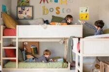 a grey kids’ room with three bunk beds, ladders, a space for hanging out, crate bookshelves and bright decor