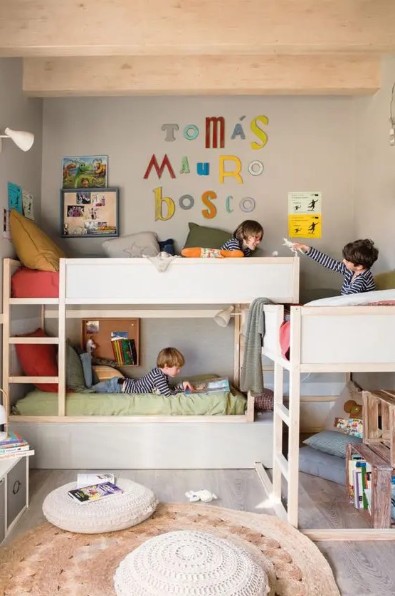 a grey kids' room with three bunk beds, ladders, a space for hanging out, crate bookshelves and bright decor