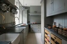 a grey kitchen with shaker panel and shaker cabinets, black soapstone countertops, brass fixtures and beadboard backsplashes