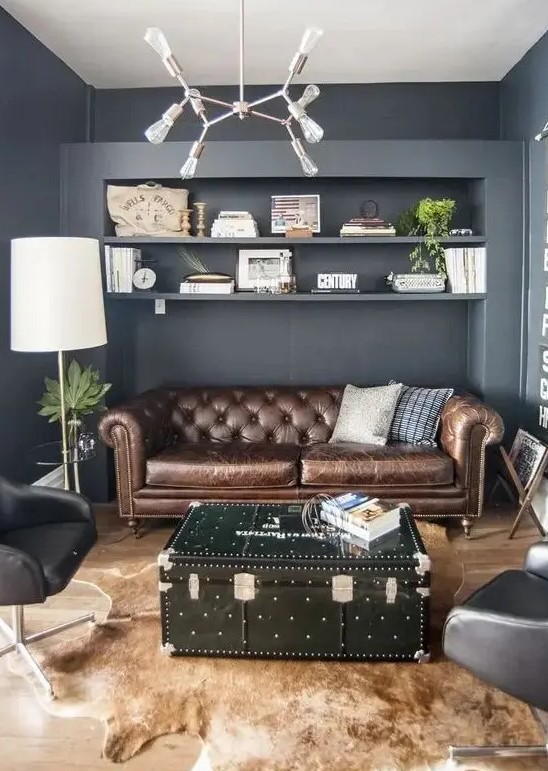 a grey living room with a brown leather Chesterfield, black chairs, a black chest as a coffee table and an animal skin rug