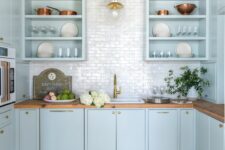 a light blue kitchen with open and flat panel cabinets, butcherblock countertops, a white tile backsplash and pendant lamps