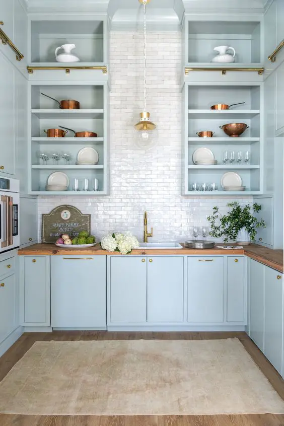 a light blue kitchen with open and flat panel cabinets, butcherblock countertops, a white tile backsplash and pendant lamps