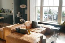 a light-filled living room with an oversized tan leather low sofa, printed pillows and some lamps and decor