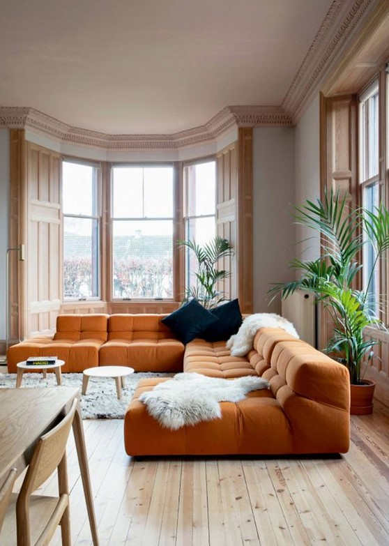 a light filled living room with gorgeous views of the city, an orange sectional, round coffee tables and dark pillows