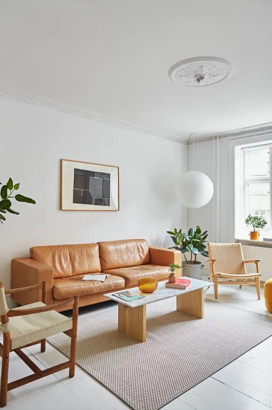 a light filled mid century modern living room with an amber leather sofa, neutral chairs and a simple coffee table, a pendant lamp