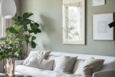 a lovely living room with a sage green accent wall, a white sofa and neutral pillows, a gallery wall, a round coffee table and potted plants