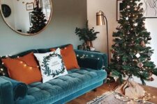 a lovely living room with a turquoise sofa, a Christmas tree with lights, a floor lamp and a round mirror plus a printed rug