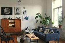 a mid-century modern living room with a blue sofa, a stained buffet, a black rocker, a low bench, a basket for storage and a cool gallery wall