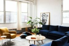 a mid-century modern living room with a navy sectional, a mustard chair, a coffee and a side table and some greenery