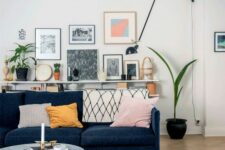 a mid-century modern living room with a navy sofa, a coffee table, a ledge gallery wall, potted plants and a black lamp