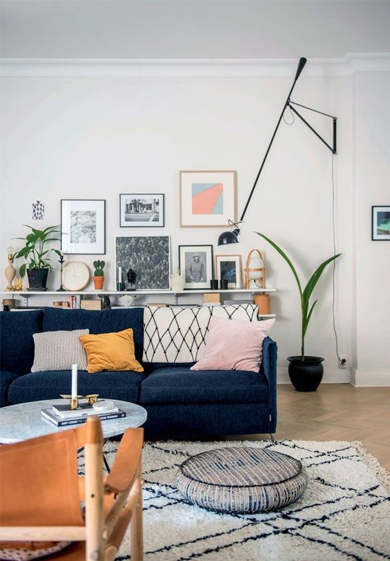 a mid century modern living room with a navy sofa, a coffee table, a ledge gallery wall, potted plants and a black lamp