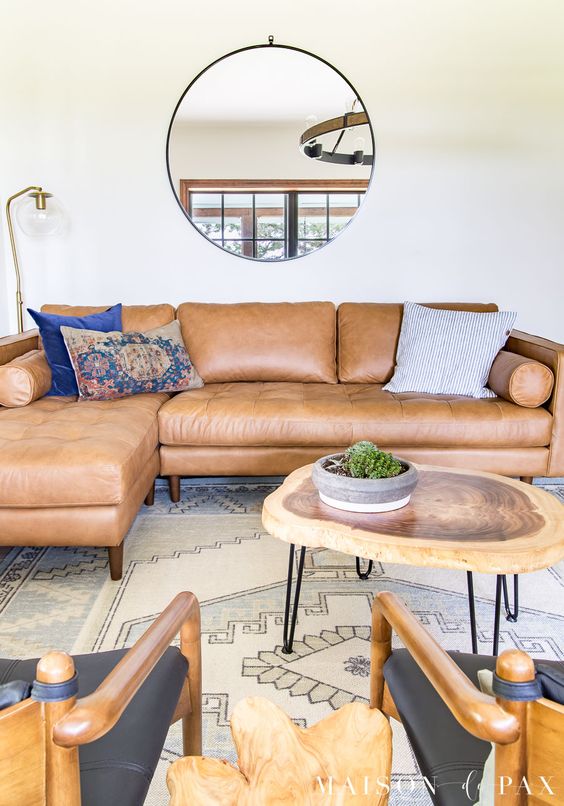 a mid century modern living room with a tan leather sectional, black chairs, a living edge coffee table and a printed rug