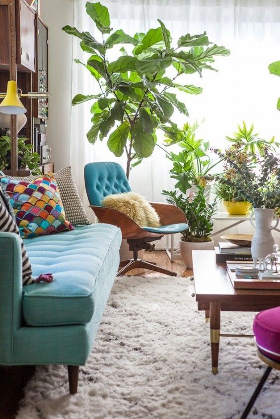 a mid century modern living room with a turquoise sofa and bright pillows, a blue chair and a coffee table, potted plants