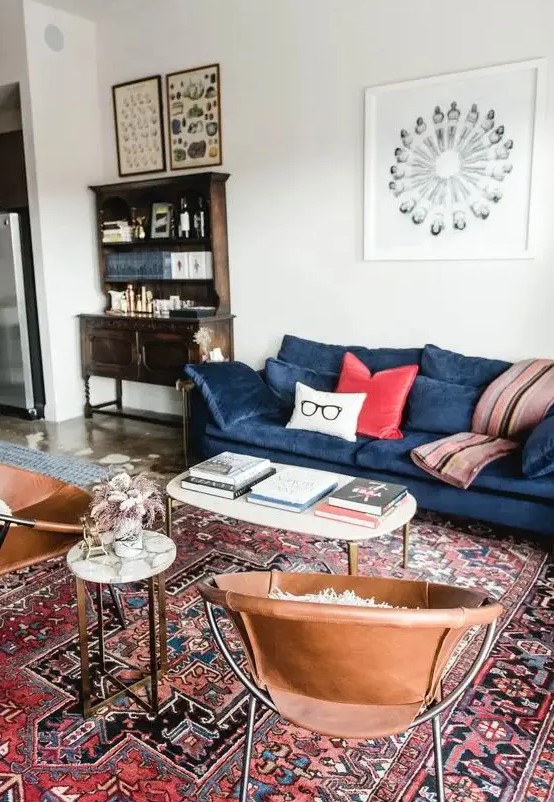 a mid-century modern living room with a vintage bureau, a modern blue sofa with colorful pillows, leather chairs, coffee tables and a red printed rug