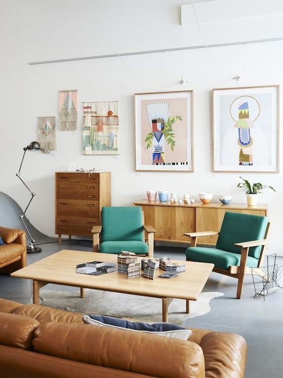 a mid-century modern living room with green chairs, a tan leather sofa, a low coffee table, stained storage funriture and a gallery wall that includes macrame