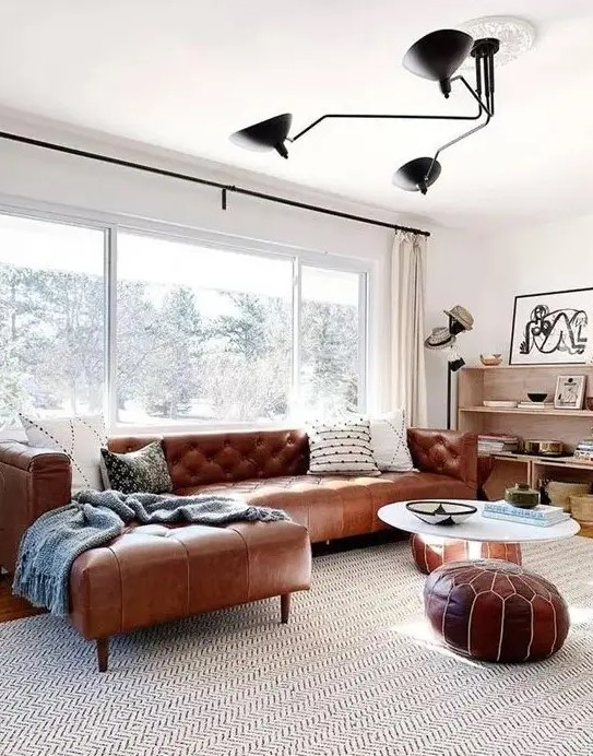 a mid century modern neutral living room with a brown leather corner sofa and matching Moroccan poufs