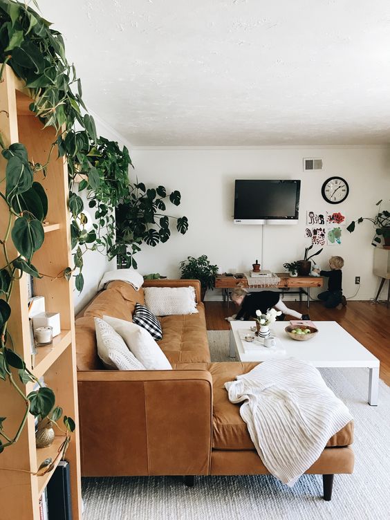 a mid century modern to boho living room with a tan leather sectional, a large coffee table, a bench and lots of potted greenery