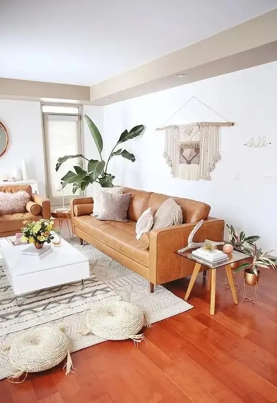 a mid century modern to boho living room with tan leather furniture, a low white coffee table, woven poufs, a macrame hanging and potted plants