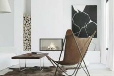 a minimal space with a built-in fireplace, firewood, a black and white artwork, a stained table and a leather butterfly chair