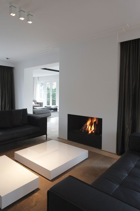 a minimalist and contrasting living room with a minimalist fireplace, black leather sofas and a duo of low white coffee tables