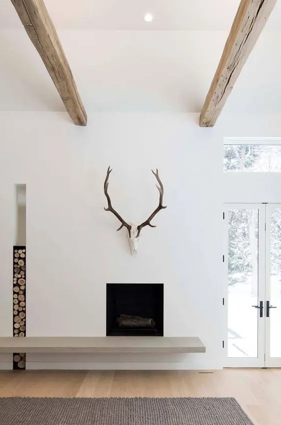 a minimalist fireplace with a concrete detail, a firewood storage niche and antlers is a great idea for a minimalist space