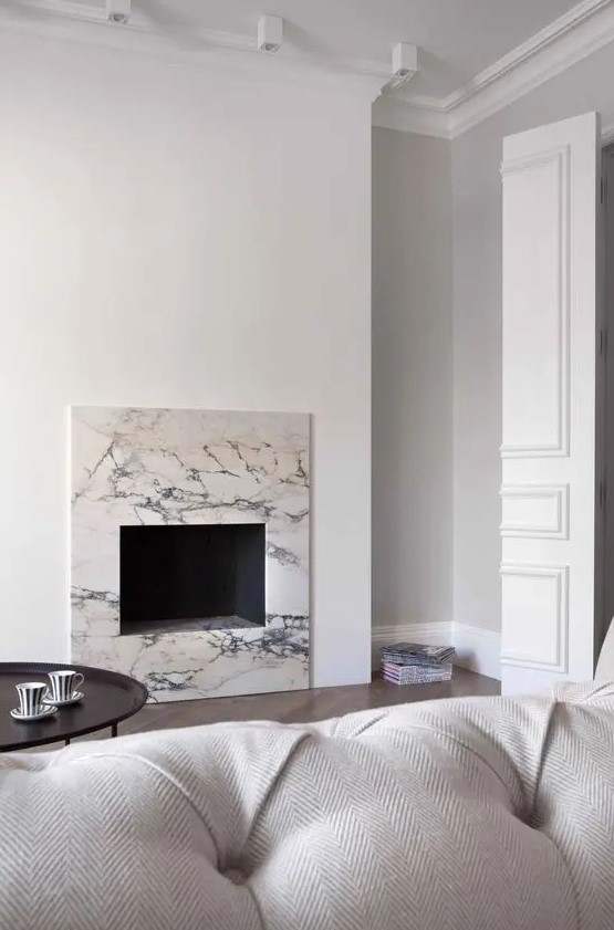 a minimalist living room with a built in fireplace surrounded with white marble, a white sofa, a dark coffee table