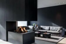 a minimalist space with a black accent wall, an ethanol fireplace under a large panel, a grey sofa, black tables