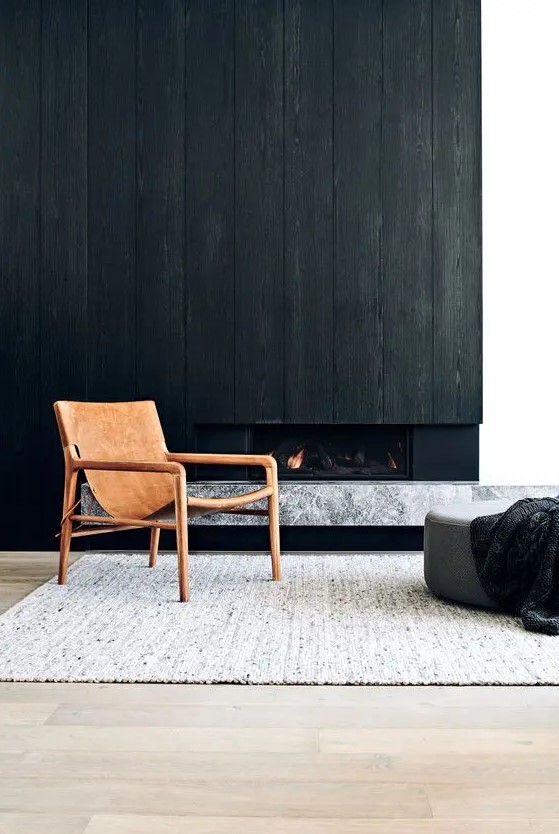 a minimalist space with a built in fireplace, a black wood cover over it, a grey marble slab, a leather chair, a grey pouf