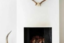 a minimalist white fireplace with a tray with pinecones, antlers, horns and other decor