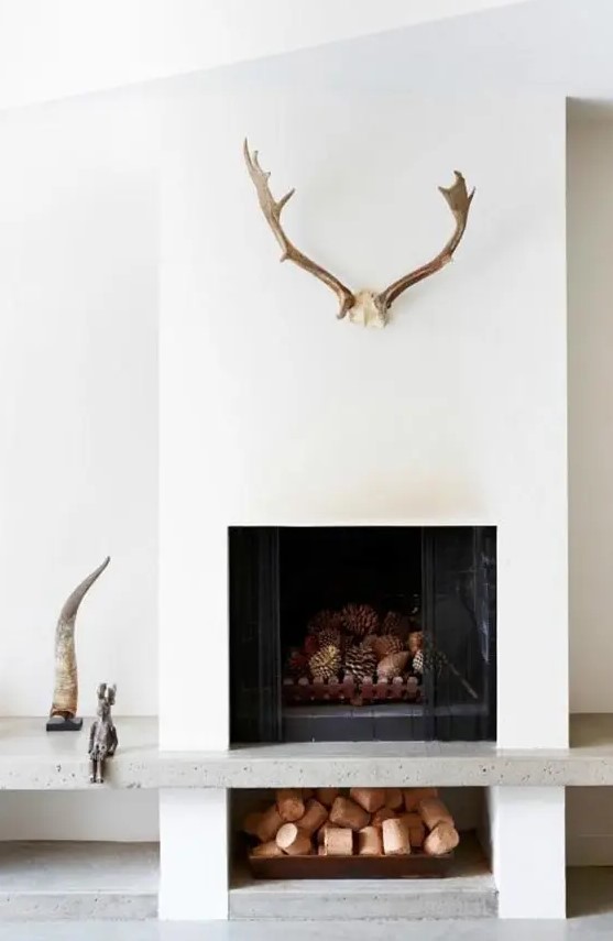 a minimalist white fireplace with a tray with pinecones, antlers, horns and other decor
