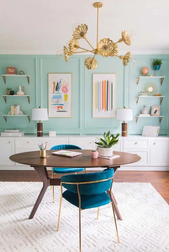 a mint blue home office with paneling, open shelves, bright artwork, a stained desk and navy chairs plus touches of gold
