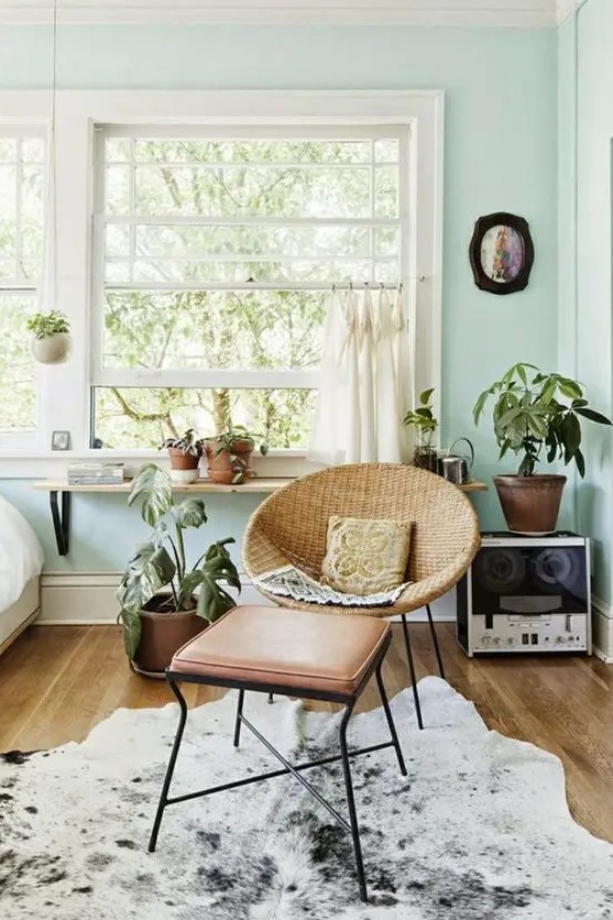 a mint blue living room with a cowhide rug, a woven chair and a leather stool, potted plants and some lovely decor