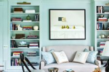 a mint blue living room with built-in shelves, a small sofa and chairs, side tables and bright artwork and blooms