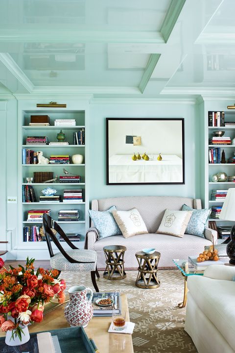 a mint blue living room with built in shelves, a small sofa and chairs, side tables and bright artwork and blooms