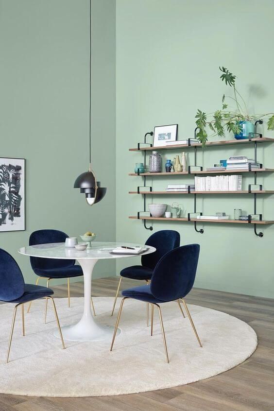 a mint green dining rom with a shelving unit, a round table and navy chairs, a round rug and a black pendant lamp