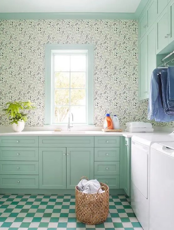 a mint green farmhouse laundry with shaker cabinets, white countertops, printed wallpaper, a green and white checked floor