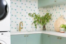 a mint green laundry room with a catchy backsplash, gold fixtures and stacked appliances is a cool space