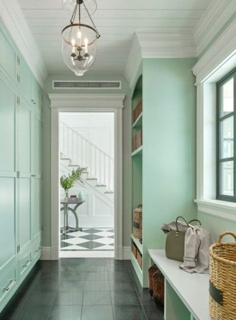 a mint green mudroom with molding on the walls, built-in storage units and a bench and a chic pendant lamp
