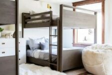 a modern boho kids’ room with stained bunk beds, neutral printed bedding, layered rugs and a white pouf