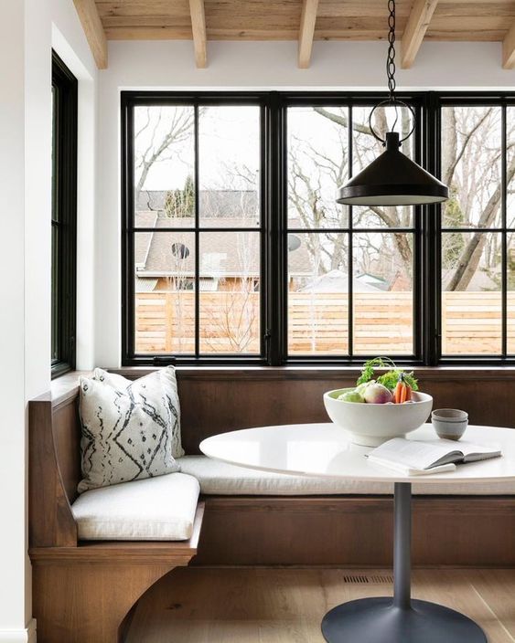 a modern breakfast corner with black casement windows, a built-in stained bench, a round table and a black pendant lamp