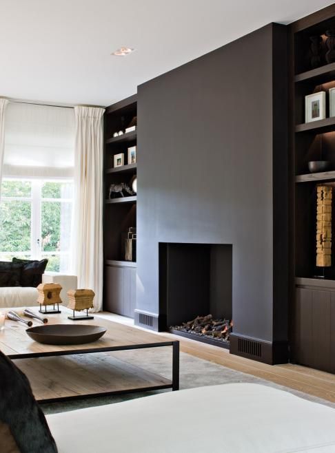 a modern dramatic living room with a minimalist black fireplace, built-in storage units, a low coffee table and creamy sofas
