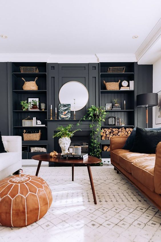 a modern farmhouse living room with a black accent wall and built-in shelves, a fireplace, an amber leather couch, a coffee table and a creamy sofa