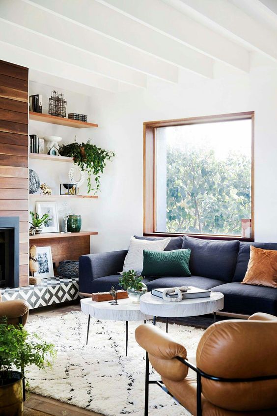 a modern farmhouse living room with a built in fireplace, a navy sofa, tan leather chair, tree slice coffee tables and shelves