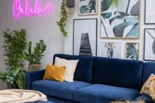 a modern living room with navy sofas, an ottoman, a botanical gallery wall, potted greenery and a pink neon sign on the wall