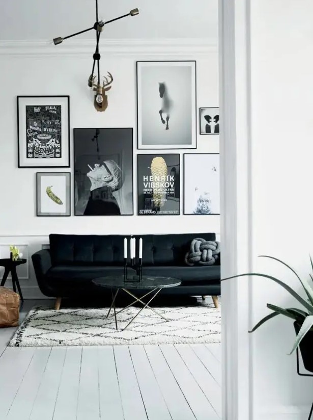 a monochromatic black and white living room with a catchy black sofa, a black and white gallery wall, a side and a coffee table and a brown leather pouf