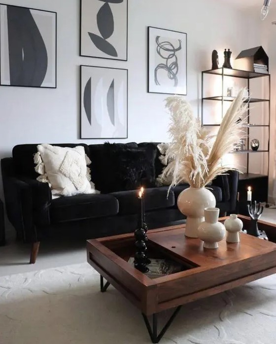 a monochromatic boho living room with a black velvet sofa, a black and white gallery wlal, a stained coffee table and a black storage unit