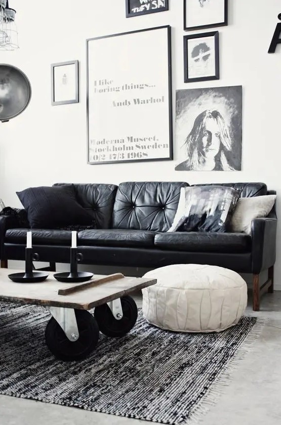 a monochromatic living room with a black leather couch, a gallery wall, an industrial coffee table on casters and a white leather pouf