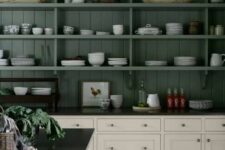a moody kitchen with open green cabinets that match the walls, creamy shaker ones and a creamy kitchen island